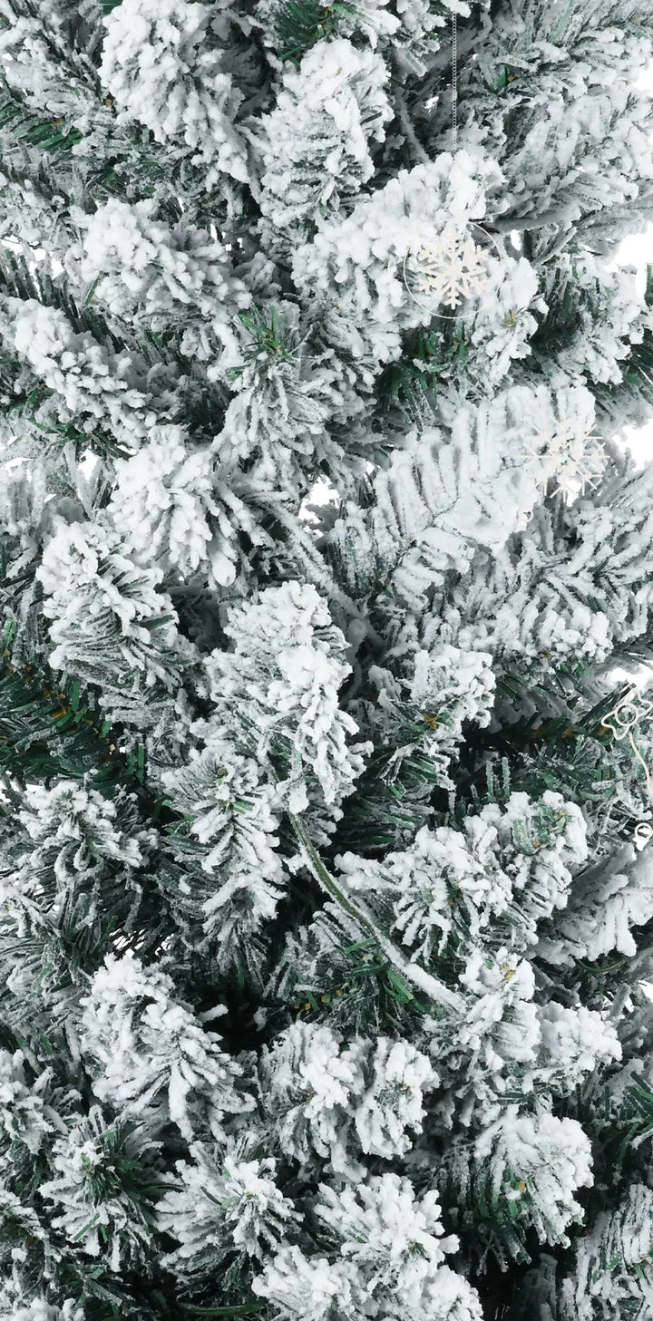 Smalt snødekt juletre med varmhvite lys i stue